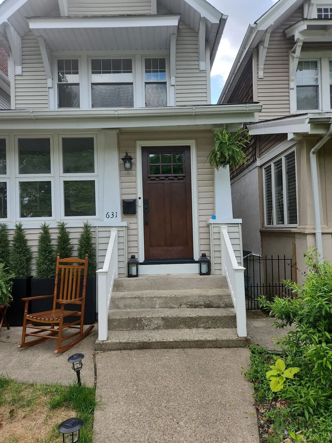 Charming house entrance with a wooden door, lanterns, and front steps. Green plants on porch.